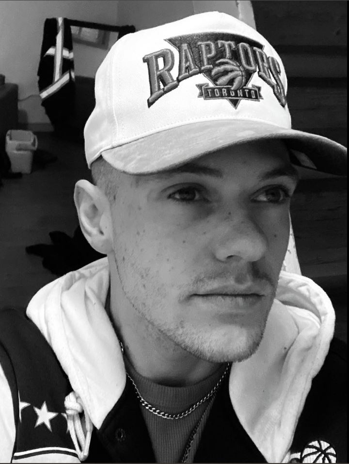 White male wearing a white toronto raptors baseball cap, a hooded sweater