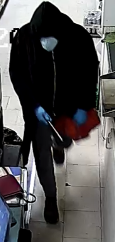 suspect wearing grey sweatpants, a black zip-up hoodie, a dark red and black knee-length plaid jacket or housecoat, blue medical gloves, and a white medical mask