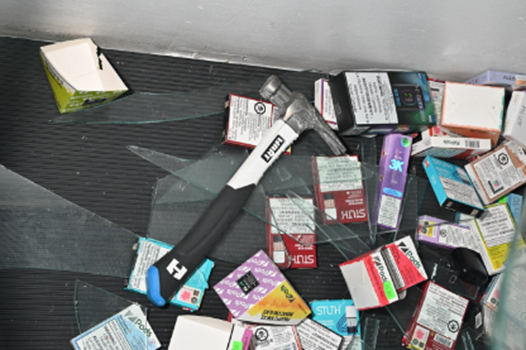 Hammer, broken glass, and boxes of product on ground