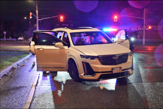 White Cadillac SUV with police cruiser behind it