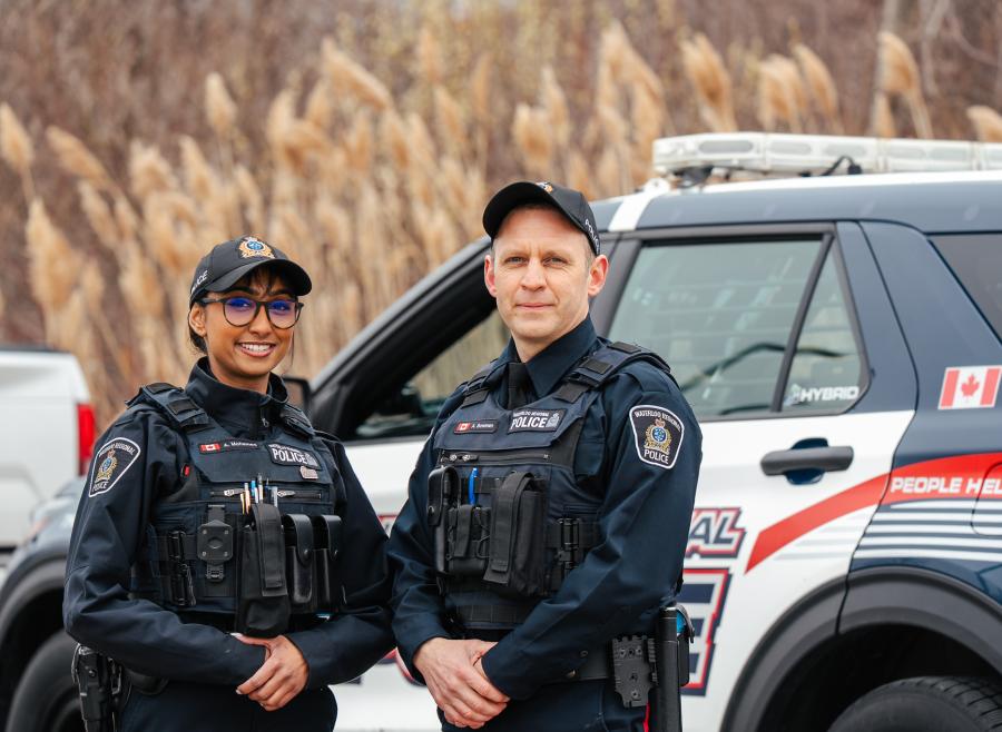 Two police officers in front of cruiser. 